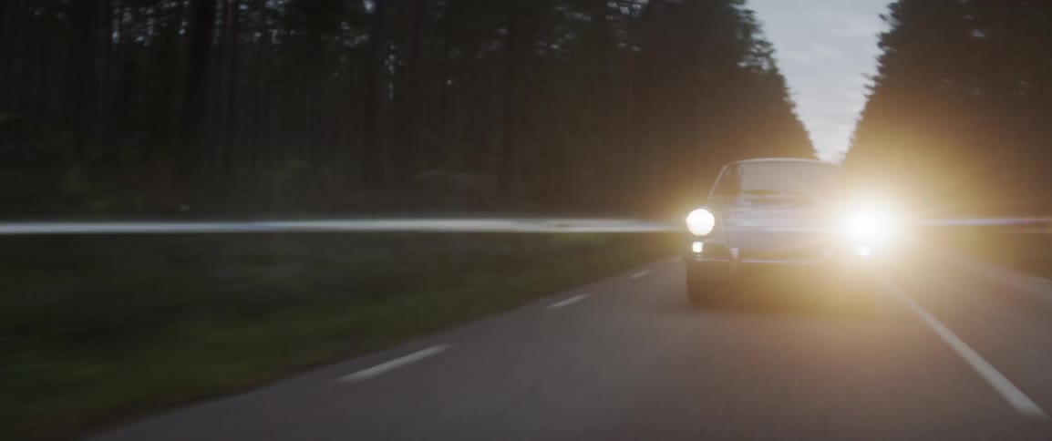 An old sports car drives on the rural road at night
