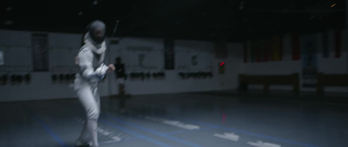 A person is fencing in the dark gym