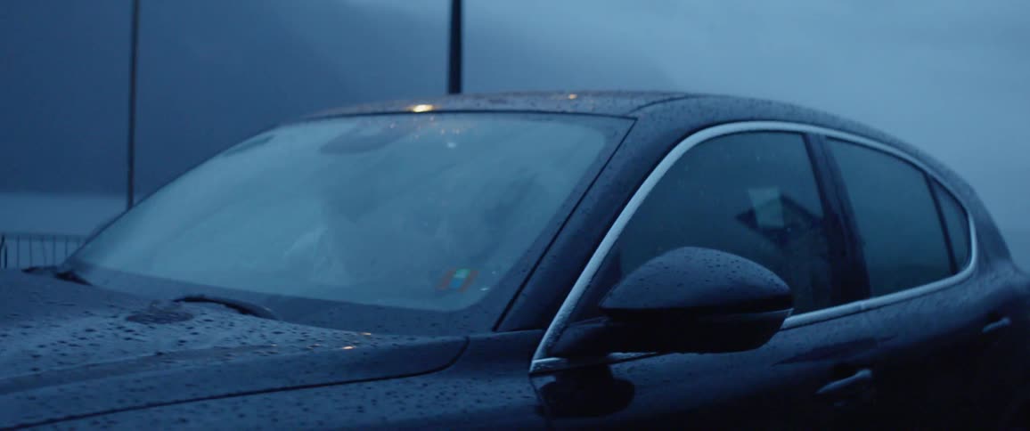 A parked car's headlights are reflected on the wet ground in the rain