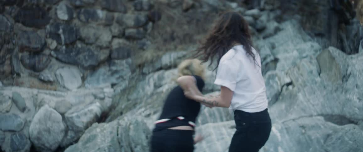 Woman grabs another woman's hand and they run across large rocks