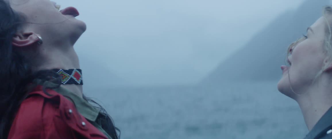 Two women laugh by the shore as it rains