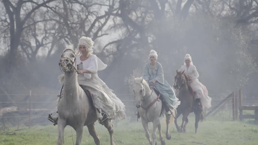Four women in white wigs and gowns ride galloping horses