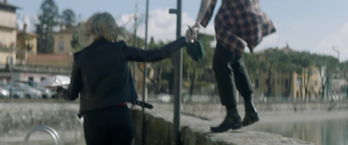 Woman holds hand of woman who is walking on a stone barrier