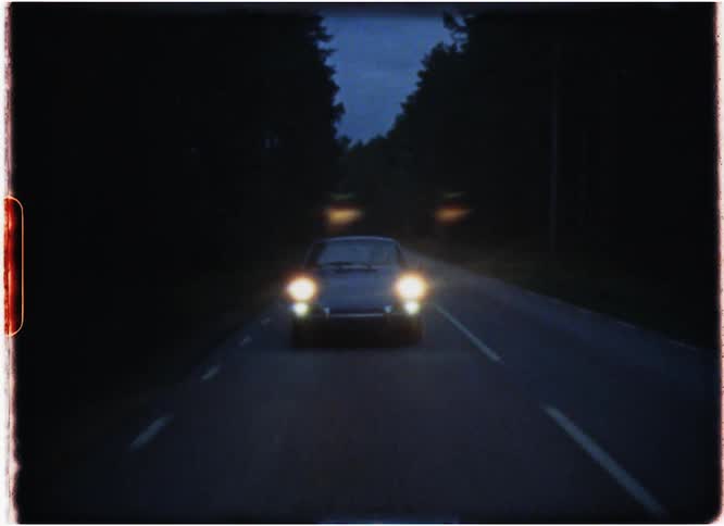 Car with its headlights on travels down the highway at night