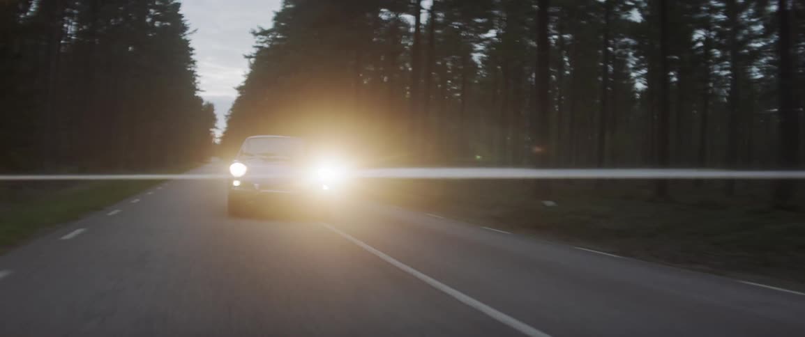 Lights shine from a car going down a road at sunset
