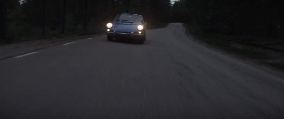 A car with headlights on travels on a rural road at dusk