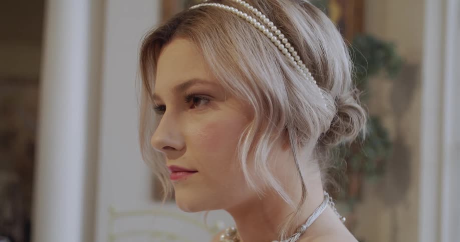 Woman with pearl headband gazes forward