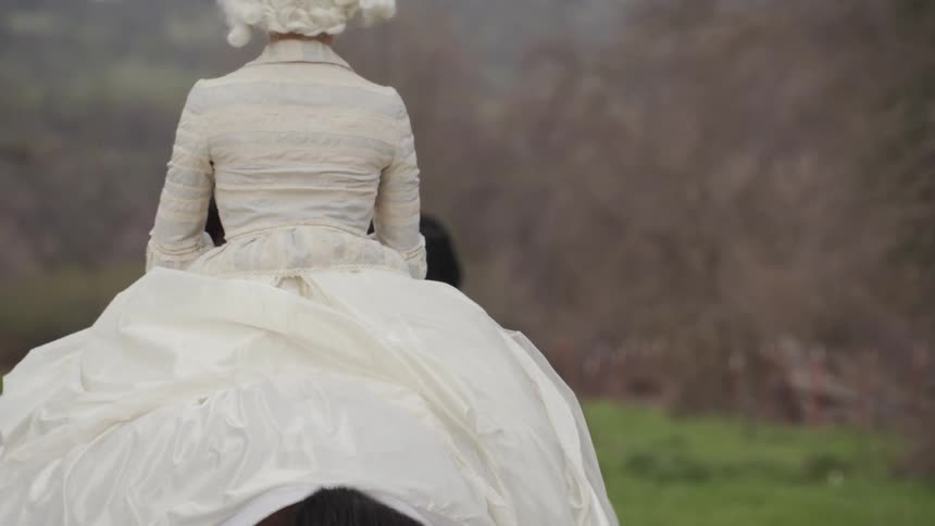 A woman wearing a white dress rides a horse