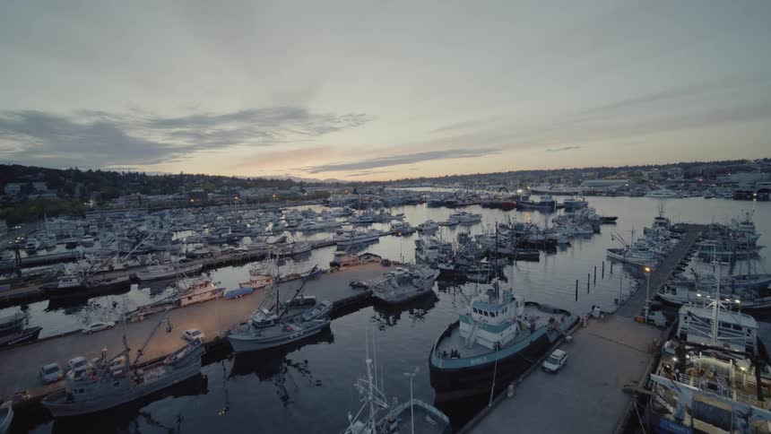 Low traverse over a variety of commercial vessels docked at an industrial marina at sunset