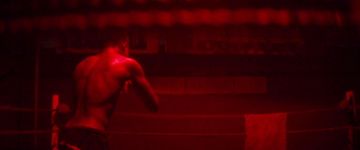 A man is shadowboxing in the dark of the ring