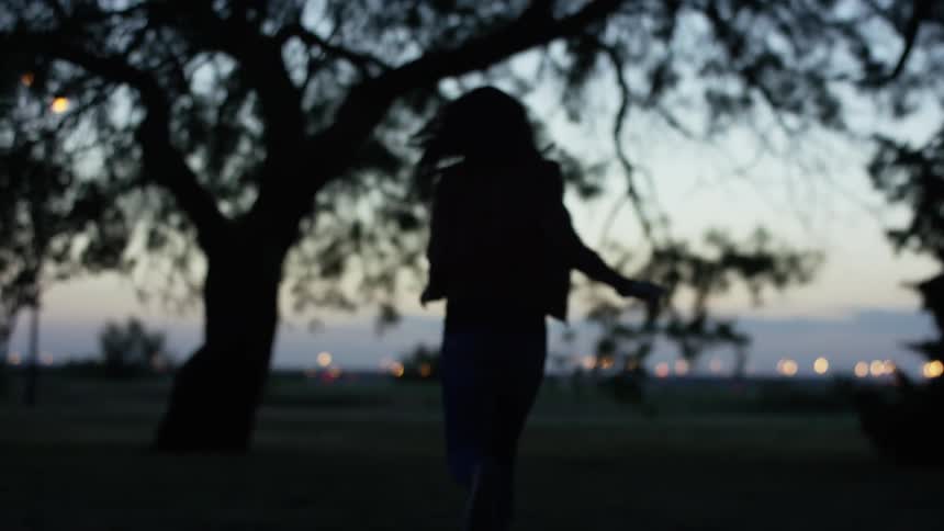 A woman runs in a field near a tree in the evening