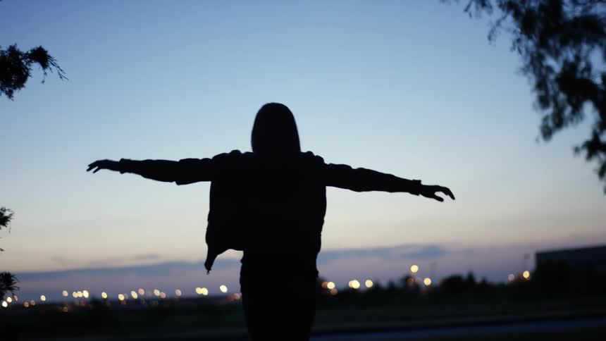 The silhouette of a man is seen with arms outstretched with the horizon in the background