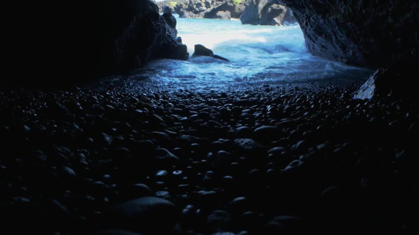 Rocks line the ground in a cave as waves splash in