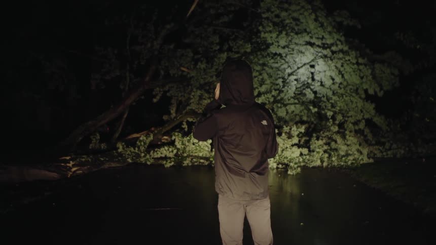 A man makes a phone call while shining a flashlight in dark woods