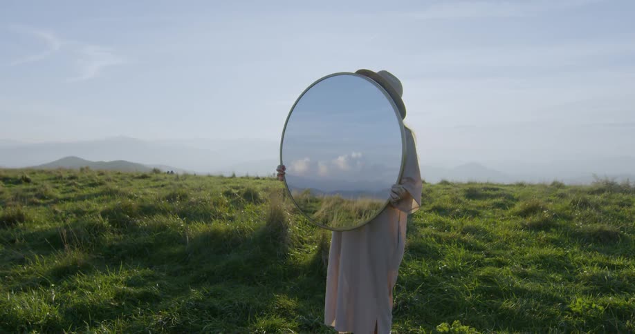 The woman is holding a large mirror in the field