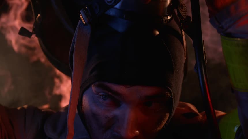 A firefighter is removing his mask as he stands in a smoky setting