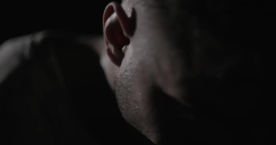 A man clenches his jaw in a dark room