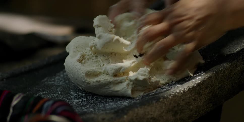 A person kneads tortilla dough on a stone