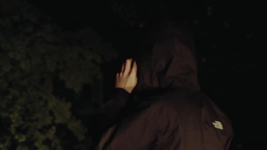 A man talks on his phone while using a flashlight at night