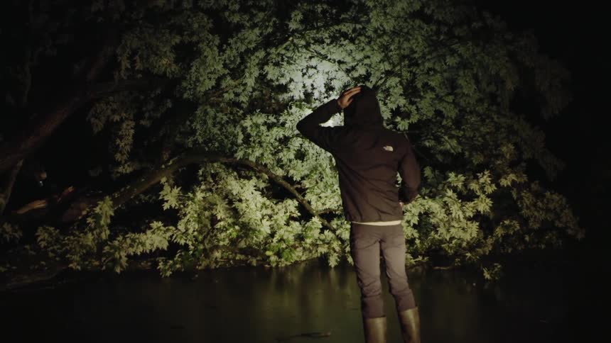 Man in a hooded jacket stands in the dark with a flashlight