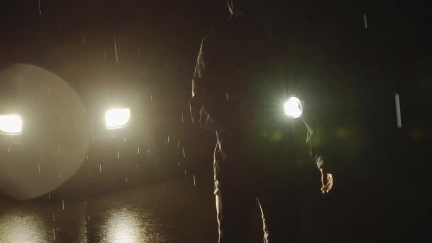 A man stands in the dark shining a flashlight in the rain
