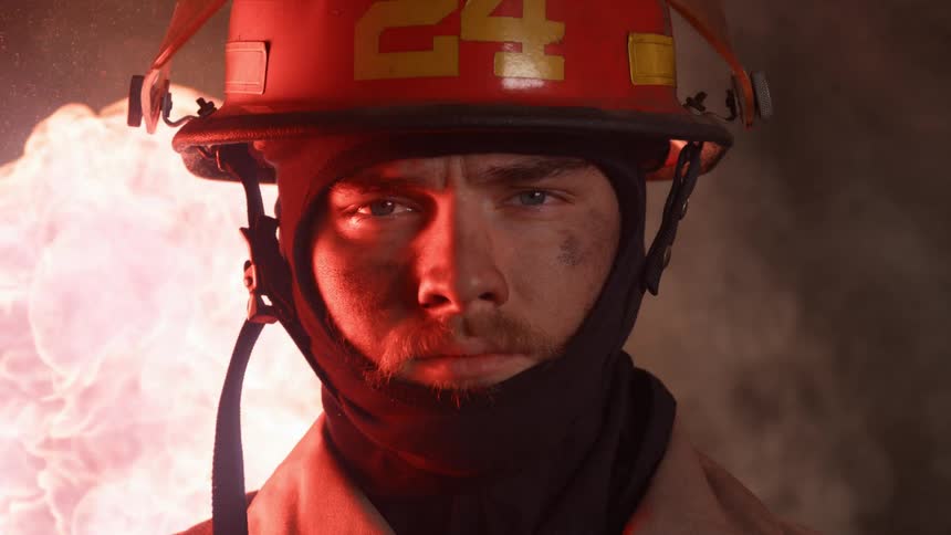 Firefighter wearing a hat stands near a burning blaze