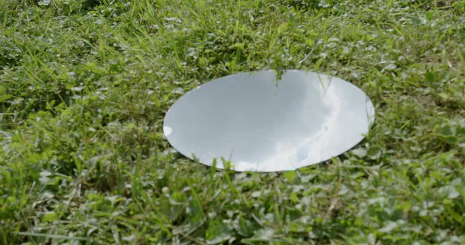 A mirror laying in the grass showing the clouds