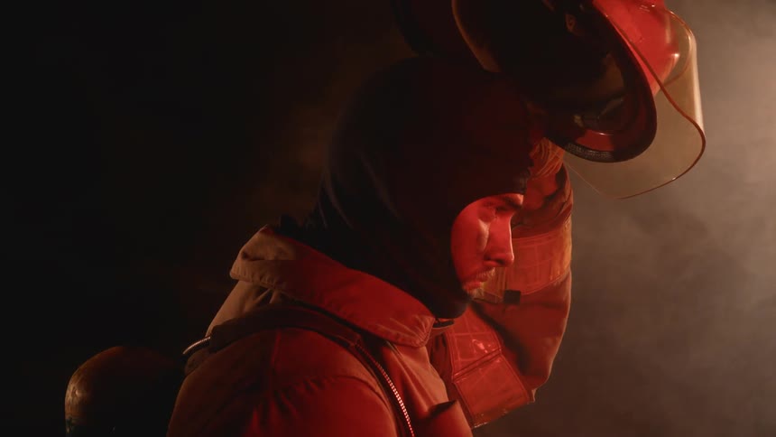A firefighter puts on a helmet with flames and smoke surrounding him