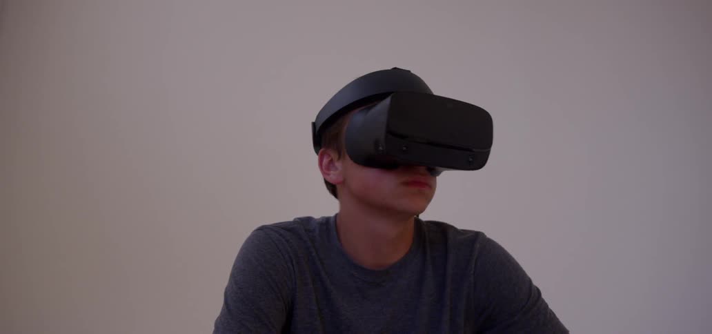 A boy is wearing a virtual reality headset while sitting outside at dusk