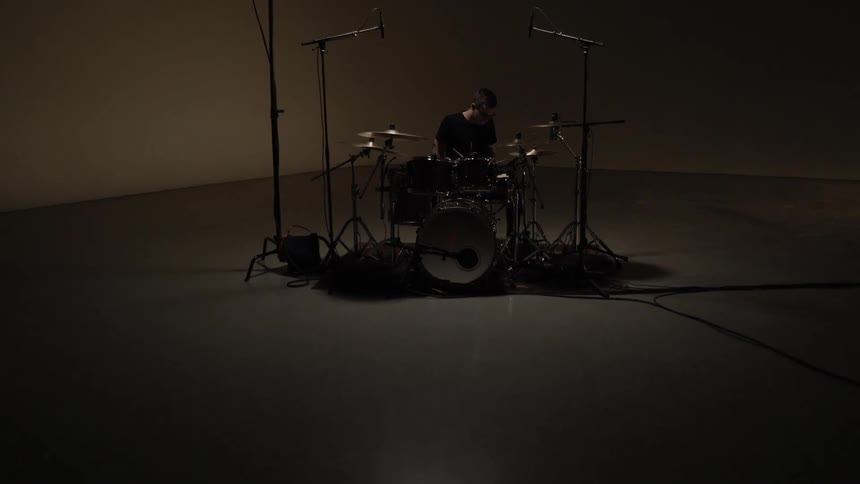 Man drums on a set in a dim room