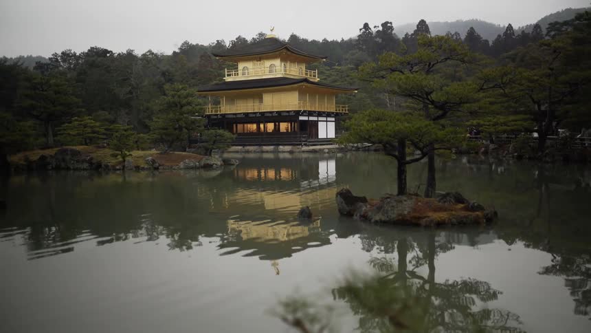 The water flows in front of the golden pavilion on an overcast day