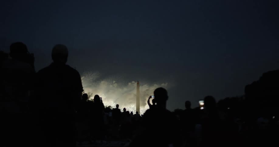 Crowd of people stand outside watching fireworks at night