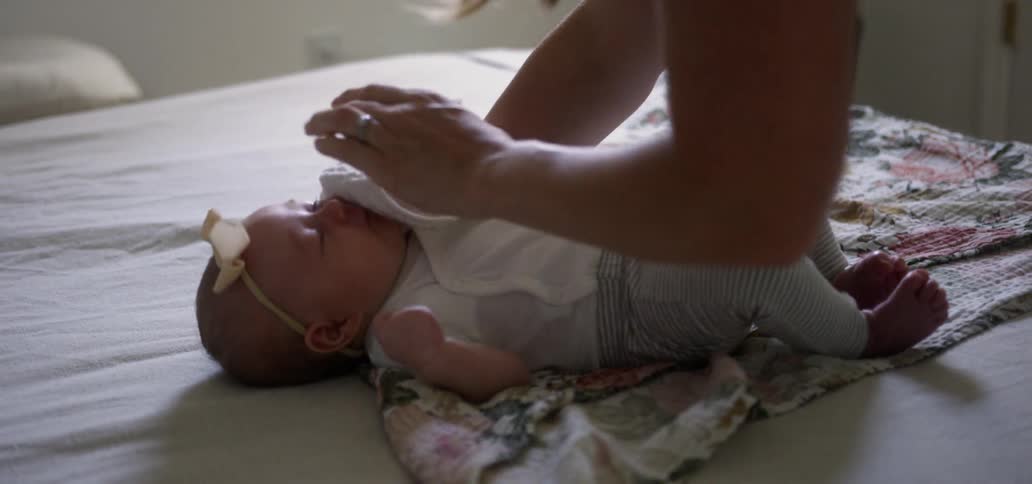 A mother is laying her baby on a bed indoors in daylight