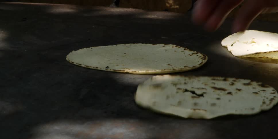 A woman is flipping tortillas on a hotplate outside in daylight