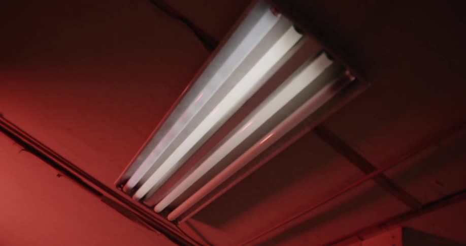 Overhead lights blink and flash in a room illuminated by red light