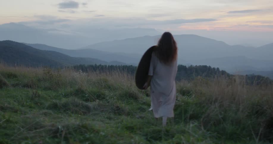 A woman walks in a rural field at sunset