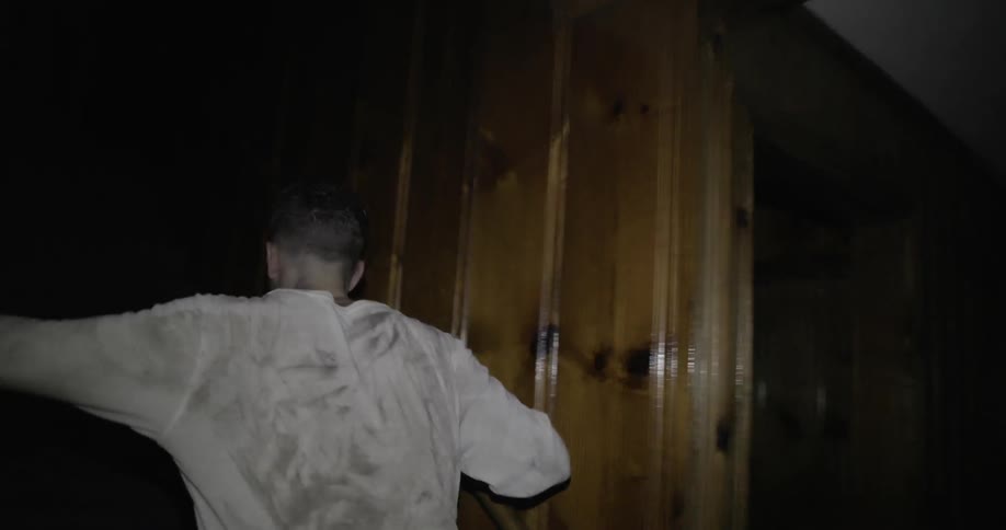 A man walks through a dark house and up the stairs
