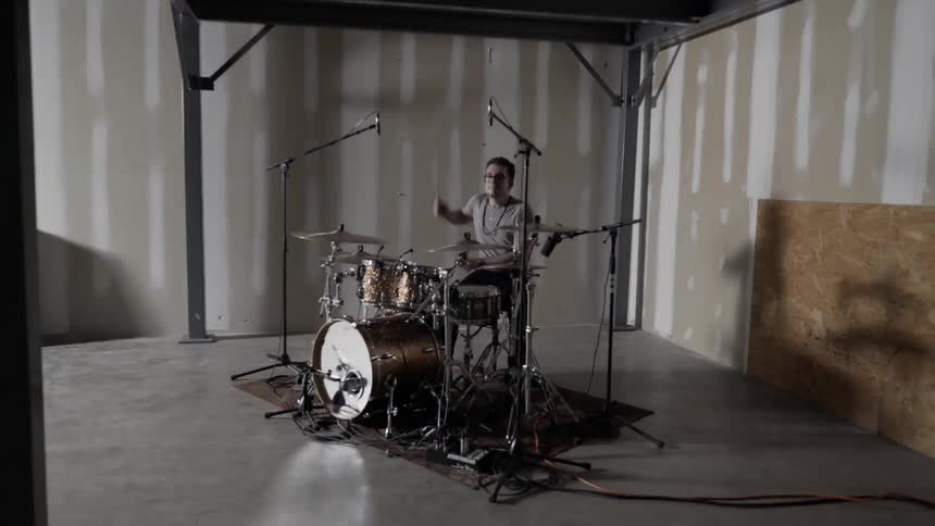 Person drums on a drum set in an empty room