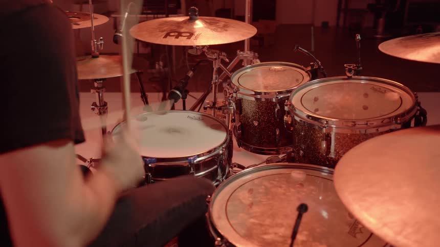 Man plays the drums as he sits on a stool