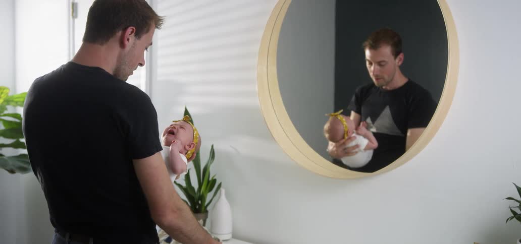 Man stands in front of mirror drying infant