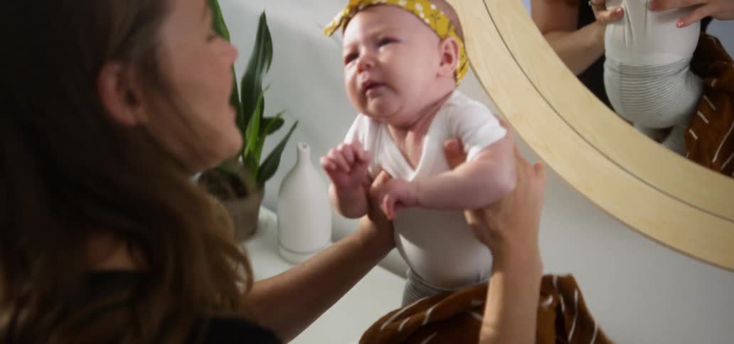 A mother is picking up her baby inside in daylight