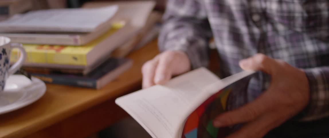 Man wearing glasses holds a paperback book