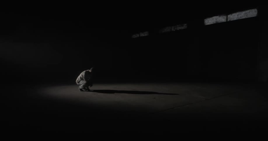 A man walks into a dark empty room and squats down
