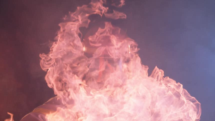 A firefighter is walking through a column of flames and smoke at night