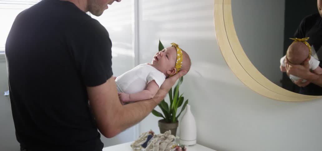 A man rocks a baby in front of a mirror