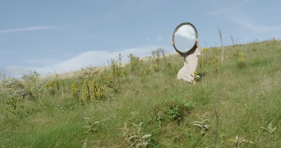 Woman standing in a field holding a mirror during the day