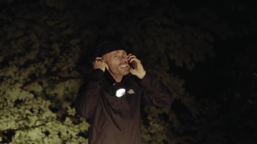 Man holds a flashlight and talks into a phone outside at night