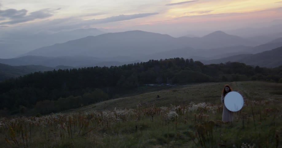 A woman holds a mirror on the side of the hill