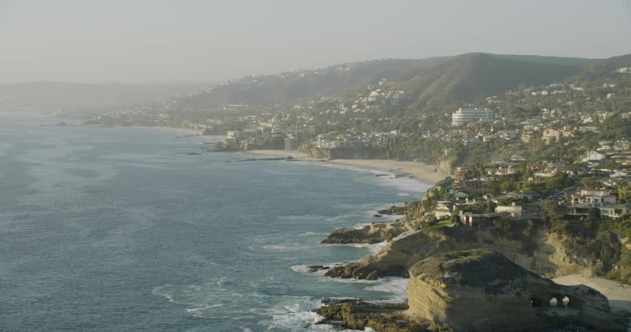 Waves crash against the cliffs at a beach in a coastal community on a hazy day