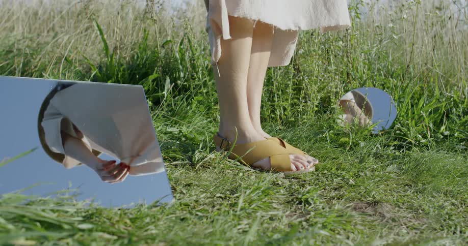 A woman stands by two mirrors in the grass